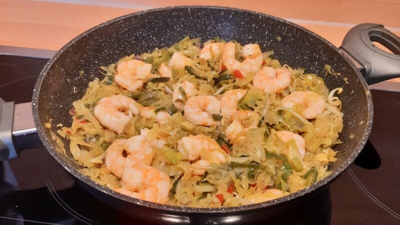 Pittig groentepannetje van spitskool, prei en paprika met grote garnalen