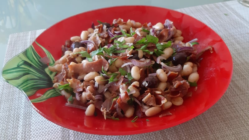 Witte bonensalade met knapperig gebakken Serranoham, gedroogde tomaten, olijven en dunne reepjes rode ui